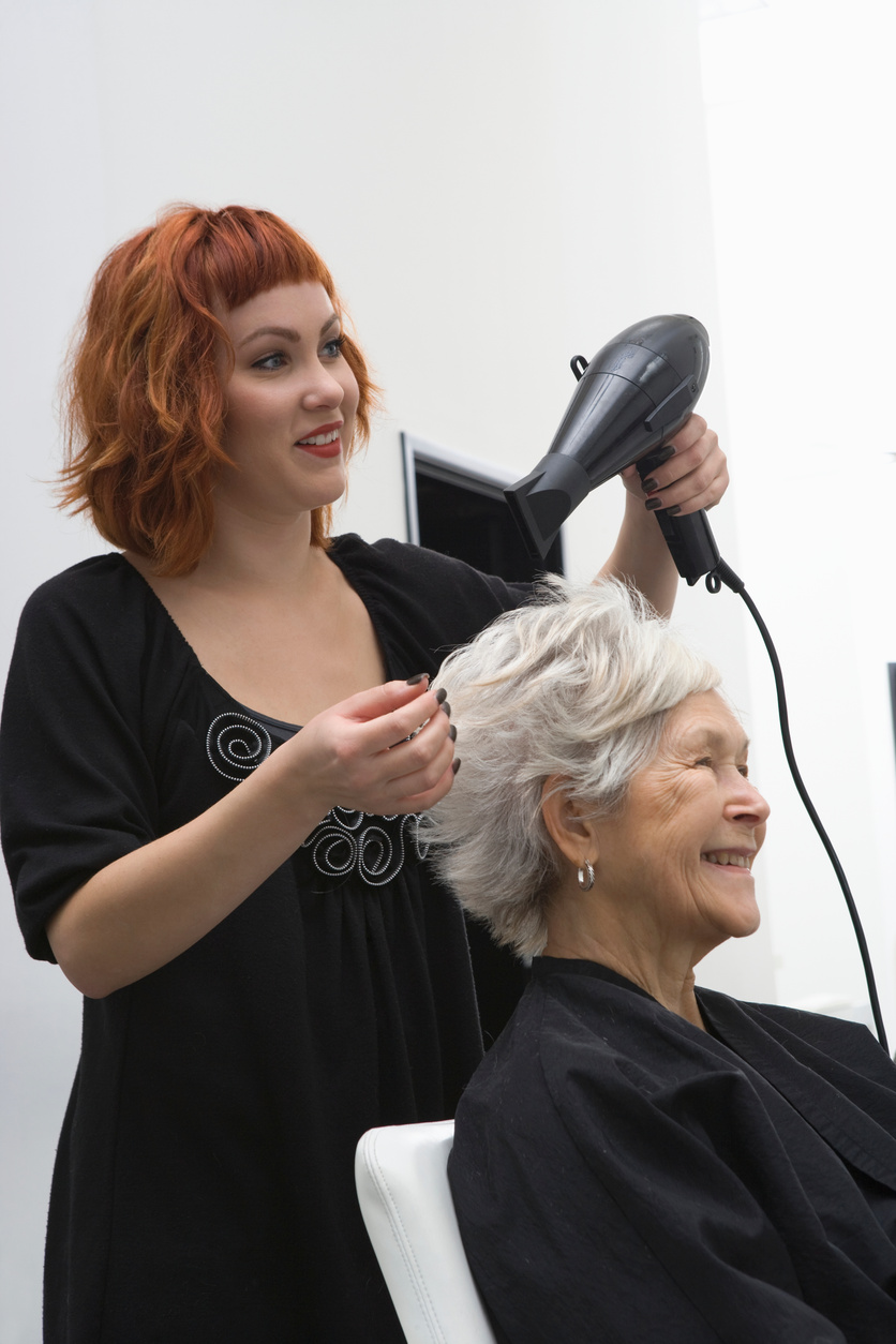 stylist blow-drys elderly woman's hair